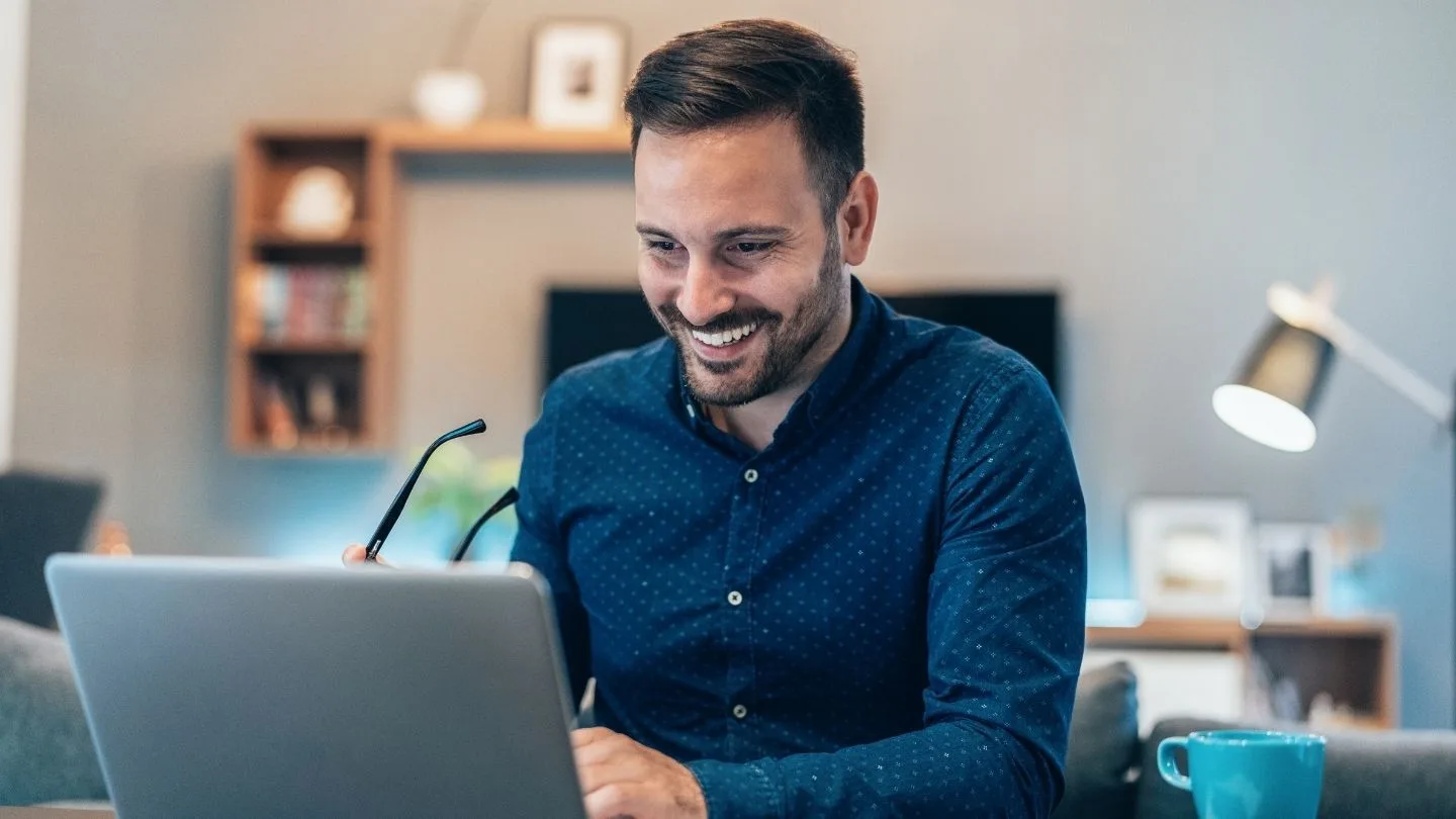uśmiechnięty mężczyzna w niebieskiej koszuli pracuje na laptopie w domu podczas home office
