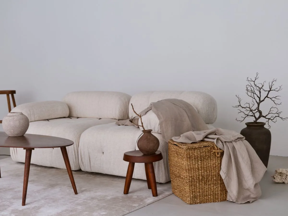 jasna sofa z lnianymi dodatkami, ciemnymi drewnianymi meblami i plecionym koszem w stylu japandi